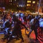 Police officers on bikes with high tech gear block protesters as other officers arrest people